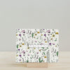 Artsy Ems Designs square seed paper card features pink, yellow & purple flowers with green leaves, on a wooden stand. The card reads Slowly growing with each pain and comes in compostable packaging.