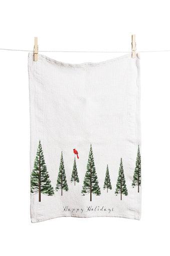 A white, 100% cotton tea towel by Artsy Ems Designs hangs on a line with clothespins, featuring illustrated evergreen trees, a red bird, and “Happy Holidays” in an artisan Christmas design.